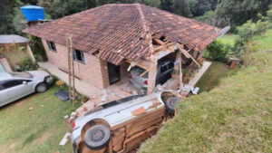 Carro atinge telhado de casa e destrói veículos após motorista perder o controle da direção